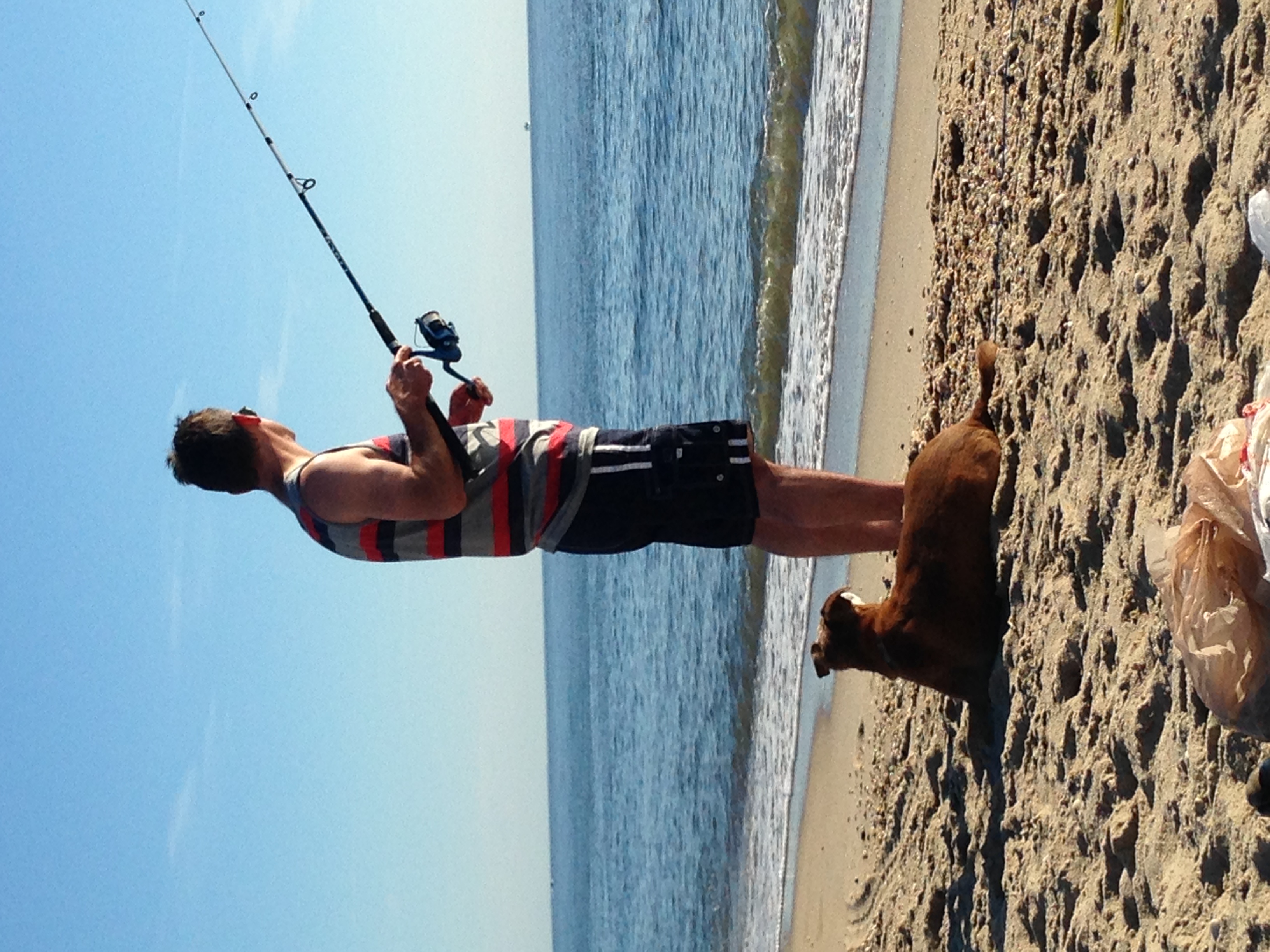 Matt Williams fishing beside the ocean with a dog resting nearby